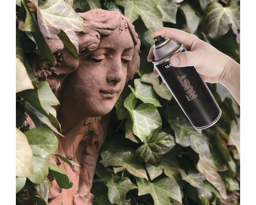 O mână pulverizează un spray cu efect de rugină pe o statuie de piatră pe fundal de iederă.