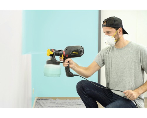 Un bărbat folosește un pistol de vopsit Wagner pentru a vopsi un perete.