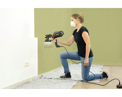 Femeie folosind un pistol de pulverizare pentru a vopsi un perete.