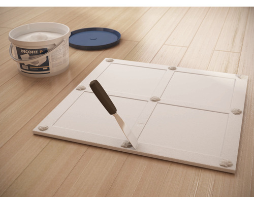 Găleată cu adeziv Decofit, spatulă și panou pe podea de lemn