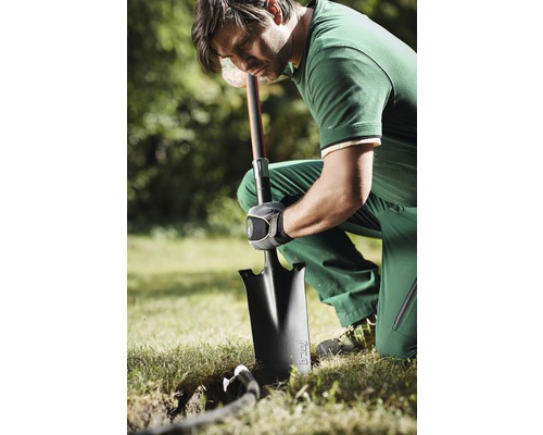 Un bărbat îngenuncheat în grădină sapă o groapă cu o lopată.