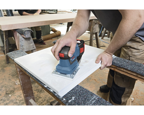 O persoană șlefuiește o scândură de lemn cu o șlefuitoare electrică cu vibrații pe un banc de lucru.