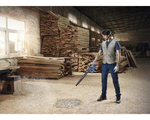 Un bărbat curăță atelierul cu un suflător de așchii de lemn.