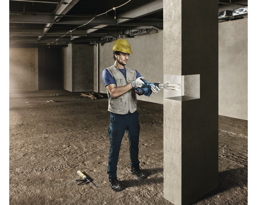 Un bărbat cu cască de protecție găurește un stâlp de beton cu un ciocan rotopercutor pe un șantier.