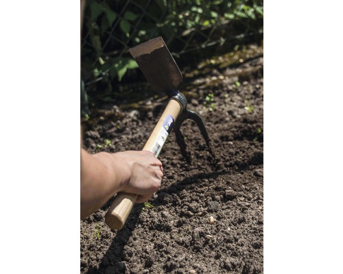 Mână ține o sapă multifuncțională în pământul din grădină