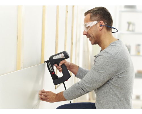 Un bărbat fixează panourile de perete cu un capsator electric pe un perete