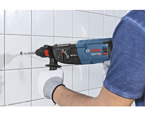 O persoană găurește un perete cu gresie cu un ciocan rotopercutor