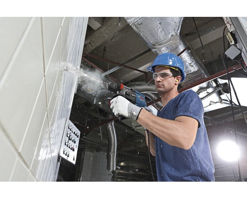 Un muncitor în construcții forează un perete cu un ciocan rotopercutor.