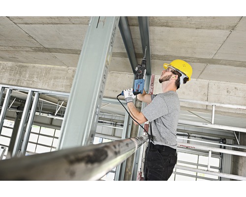 Un meșter forează cu o mașină de găurit într-un profil metalic pe un șantier.