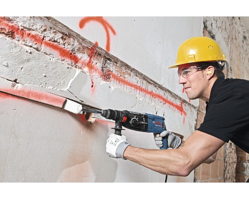 Un muncitor în construcții găurește un perete cu un ciocan rotopercutor.