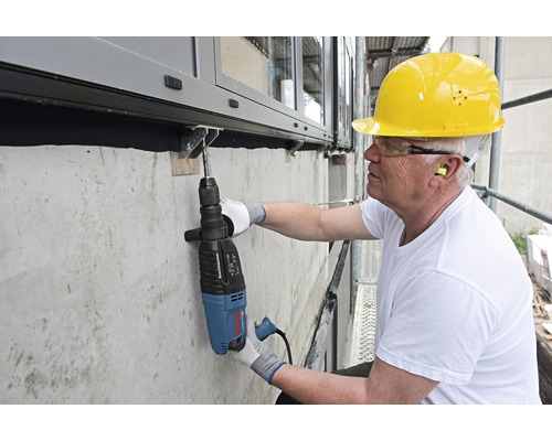 Muncitorul forează o gaură într-un perete de beton cu un ciocan rotopercutor