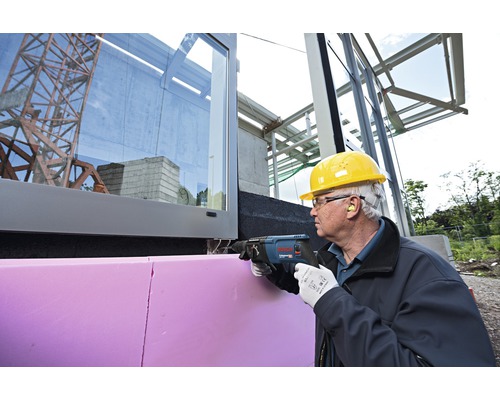 Un meșter taie o placă izolatoare pe o clădire cu un ferăstrău sabie.