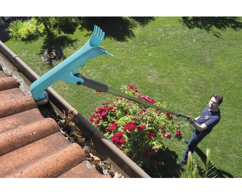 Un bărbat curăță o jgheabă cu un curățător de jgheaburi, îndepărtând frunzele.