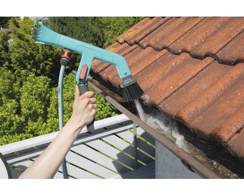 O persoană curăță o jgheabă cu o perie de jgheab și un furtun de grădină.