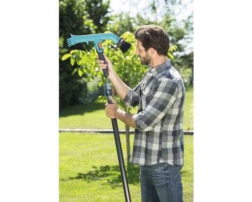 Bărbat cu o perie de grădină cu mâner telescopic în grădină.