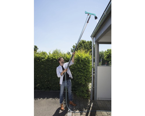 Bărbat care curăță jgheabul cu un curățător de jgheaburi și un mâner telescopic.