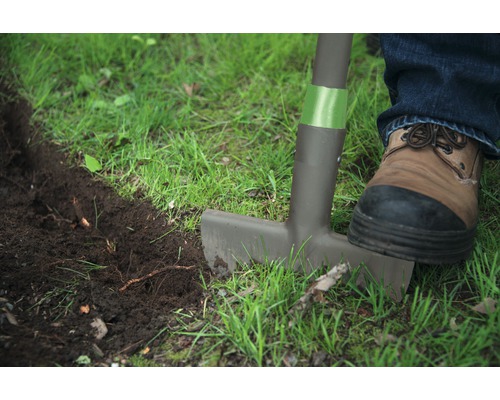 Grădinărit cu un tăietor de margini de gazon, un picior cu pantof pe tăietorul de margini de gazon