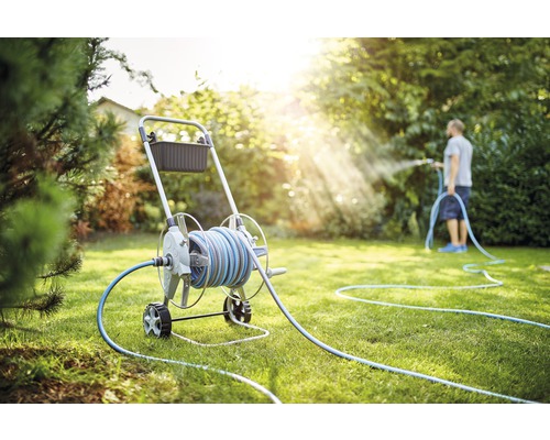 Scenă de grădină cu cărucior pentru furtun și persoană care udă gazonul