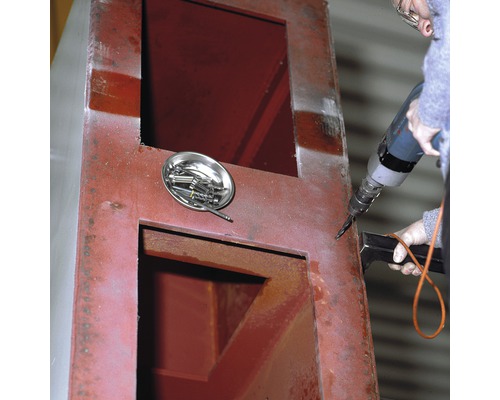 O persoană găurește o carcasă metalică cu o mașină de găurit. O tavă cu șuruburi este așezată alături.