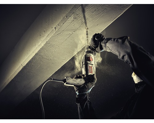 O persoană găurește un tavan de beton cu o bormașină.