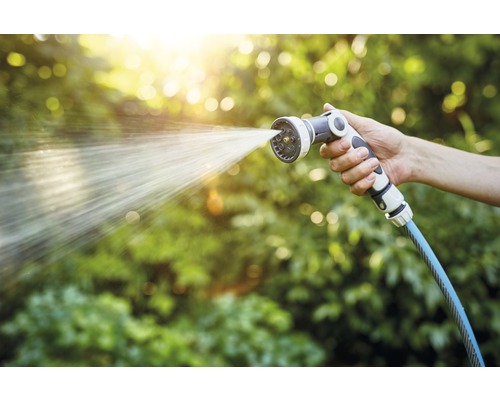 O mână ține un pistol de stropit de grădină din care iese apă