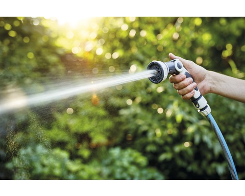 O mână ține un furtun de grădină cu cap de pulverizare, din care țâșnește apă