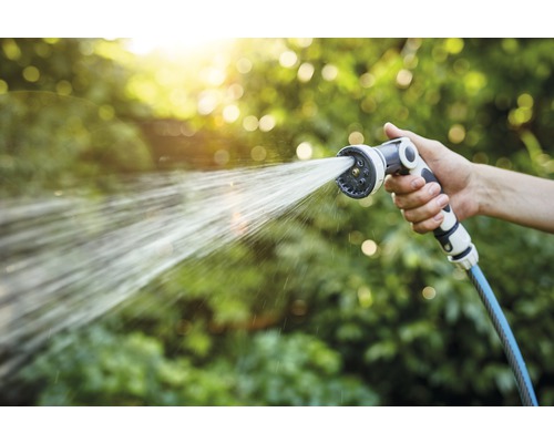 Mână ținând furtun de grădină cu cap de pulverizare care stropește cu apă