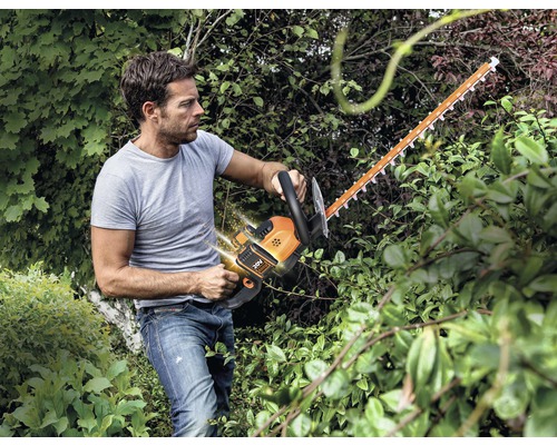 Un bărbat taie un gard viu cu o foarfecă de tuns gard viu fără fir