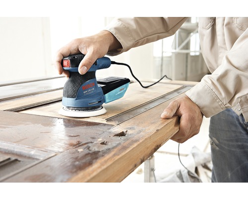 Un bărbat folosește un șlefuitor excentric Bosch pentru a șlefui o ușă din lemn.