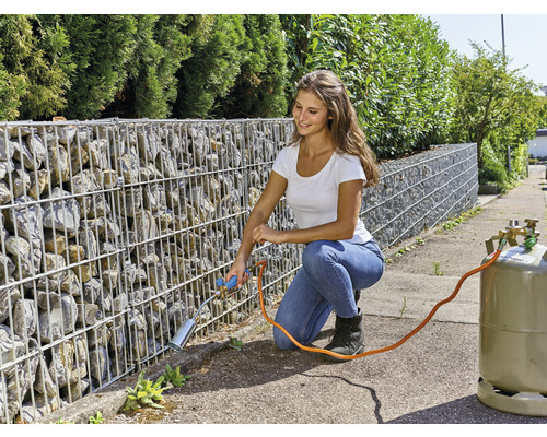 Femeie îndepărtând buruienile cu un arzător cu gaz de pe un perete de gabion