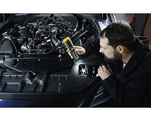 Un bărbat inspectează un compartiment motor cu o lampă de inspecție.