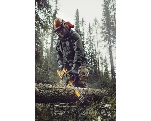 Bărbat cu echipament de protecție și drujbă tăind lemne în pădure