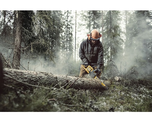 Un bărbat cu echipament de protecție taie un trunchi de copac cu un lanț într-o pădure.