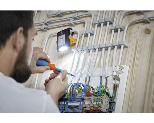 Electrician care lucrează la instalația electrică cu șurubelniță și lampă de lucru