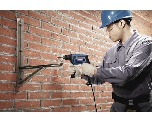 Un meșter forează cu un burghiu cu percuție într-un zid de cărămidă