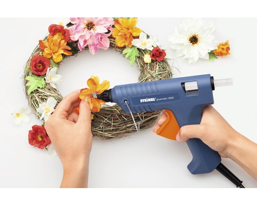 O coroană decorativă este decorată cu un pistol de lipit cu topire și flori artificiale.