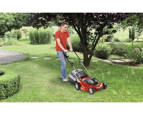 Bărbat tunde gazonul cu o mașină de tuns iarba în grădină.