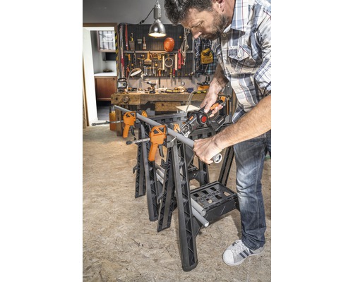 Un bărbat taie o țeavă pe un banc de lucru cu cleme și un ferăstrău sabie într-un atelier.