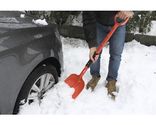O persoană spală zăpada cu o lopată de zăpadă lângă o mașină.
