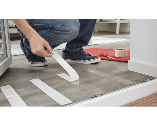 O persoană aplică bandă adezivă pe podea pentru a pregăti lucrările de renovare.