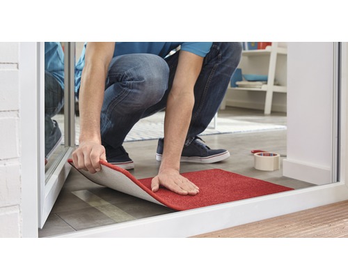 Un bărbat așază un covor roșu în intrare.