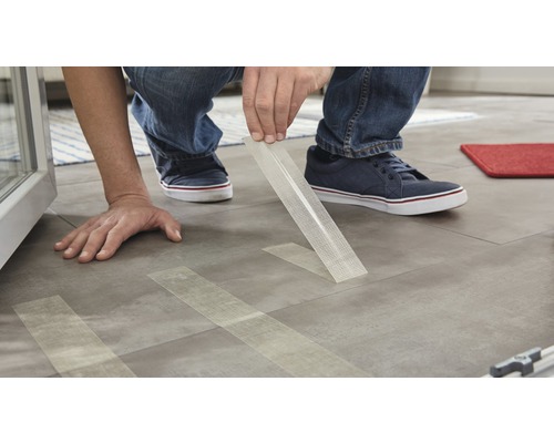 O persoană fixează bandă din țesătură de fibră de sticlă pe o podea.