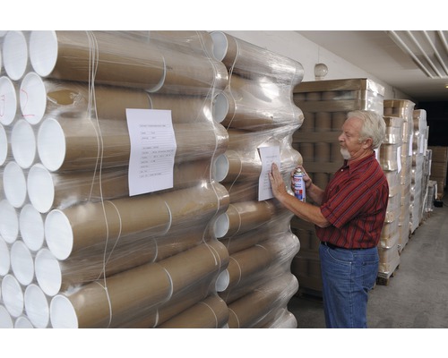 Tuburi de expediere din carton stivuite, ambalate în folie. Un bărbat ține un spray în mână.