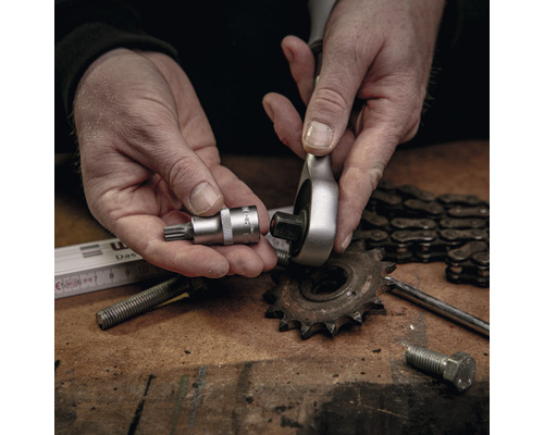 O mână ține o cheie tubulară și o mână ține o cheie cu clichet deasupra unui banc de lucru