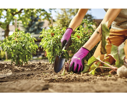 Persoană care lucrează în grădină cu o mistrie și mănuși de grădinărit.