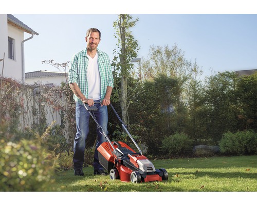 Un bărbat folosește o mașină de tuns iarba în grădină.