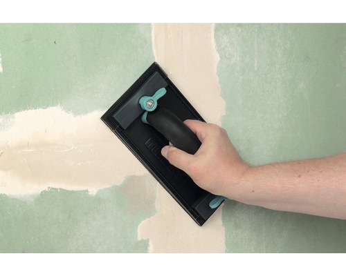 O mână șlefuiește chit pe un perete cu un șlefuitor manual