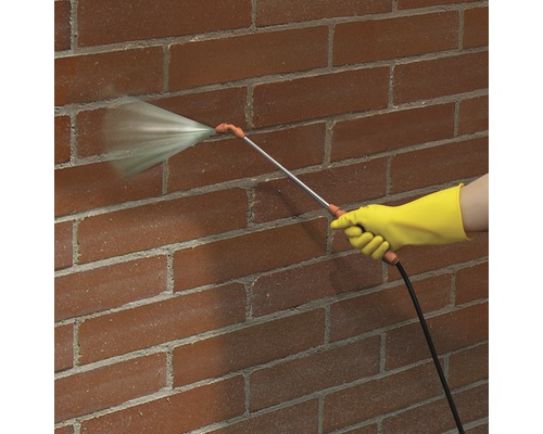 Persoană cu mănușă și pulverizator curățând un zid de cărămidă