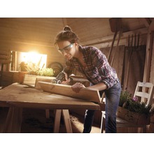 Femeie lucrând cu un ferăstrău multifuncțional într-un atelier, proiect de prelucrare a lemnului.