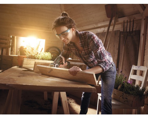 Femeie lucrând cu un ferăstrău multifuncțional într-un atelier, proiect de prelucrare a lemnului.